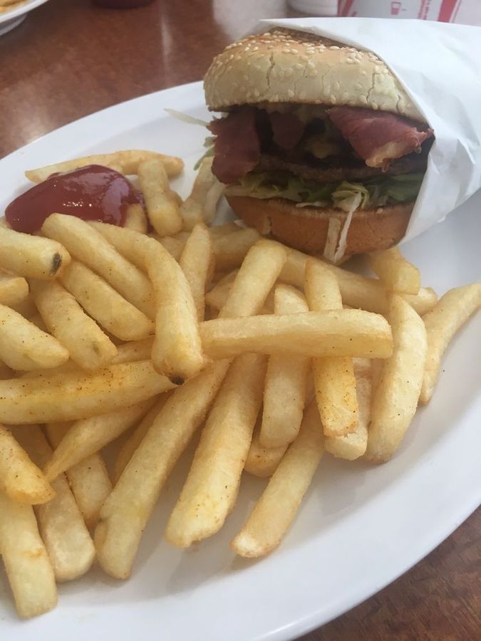 Bacon burger wrapped in paper next to a full plate of french fries with ketchup