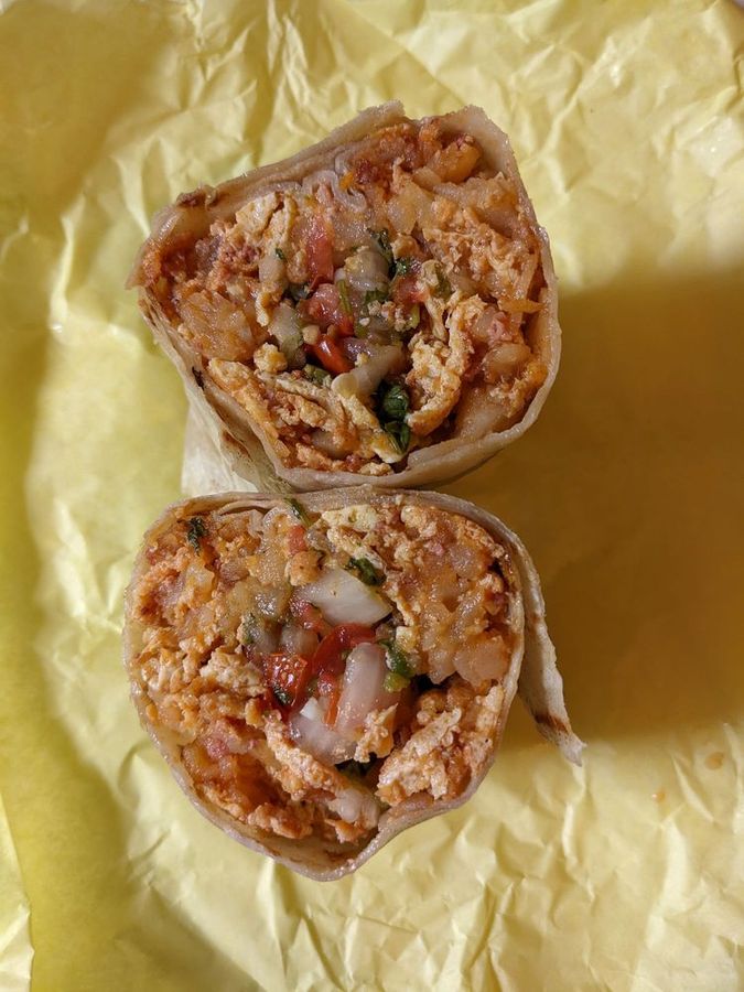 Pete&rsquo;s breakfast burrito cut in half on yellow paper, packed with scrambled eggs, potatoes, cheese, and pico de gallo