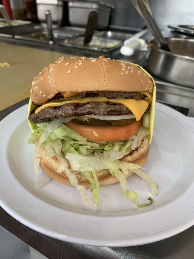 A double cheeseburger on a sesame bun with melted cheese, tomato, pickles, and shredded lettuce, fresh off the grill