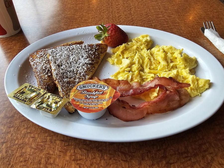 French toast breakfast plate with powdered sugar, scrambled eggs, bacon, and a strawberry