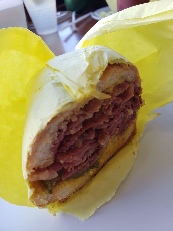 Pastrami sandwich piled high with thin-sliced pastrami and pickles, wrapped in yellow paper